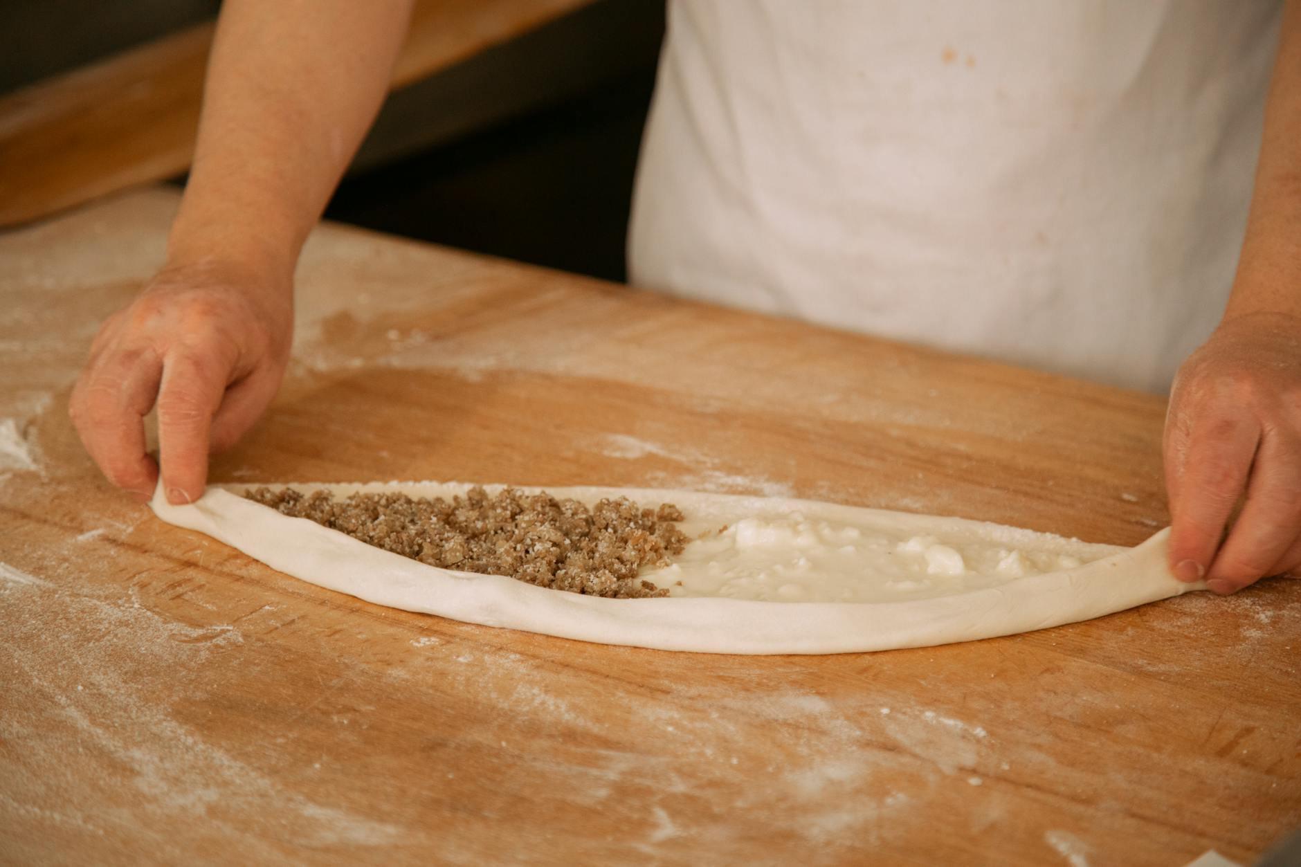 요리사가 나무 도마 위에서 길쭉한 반죽에 다진 고기와 치즈 속을 채워 피데를 만드는 모습
