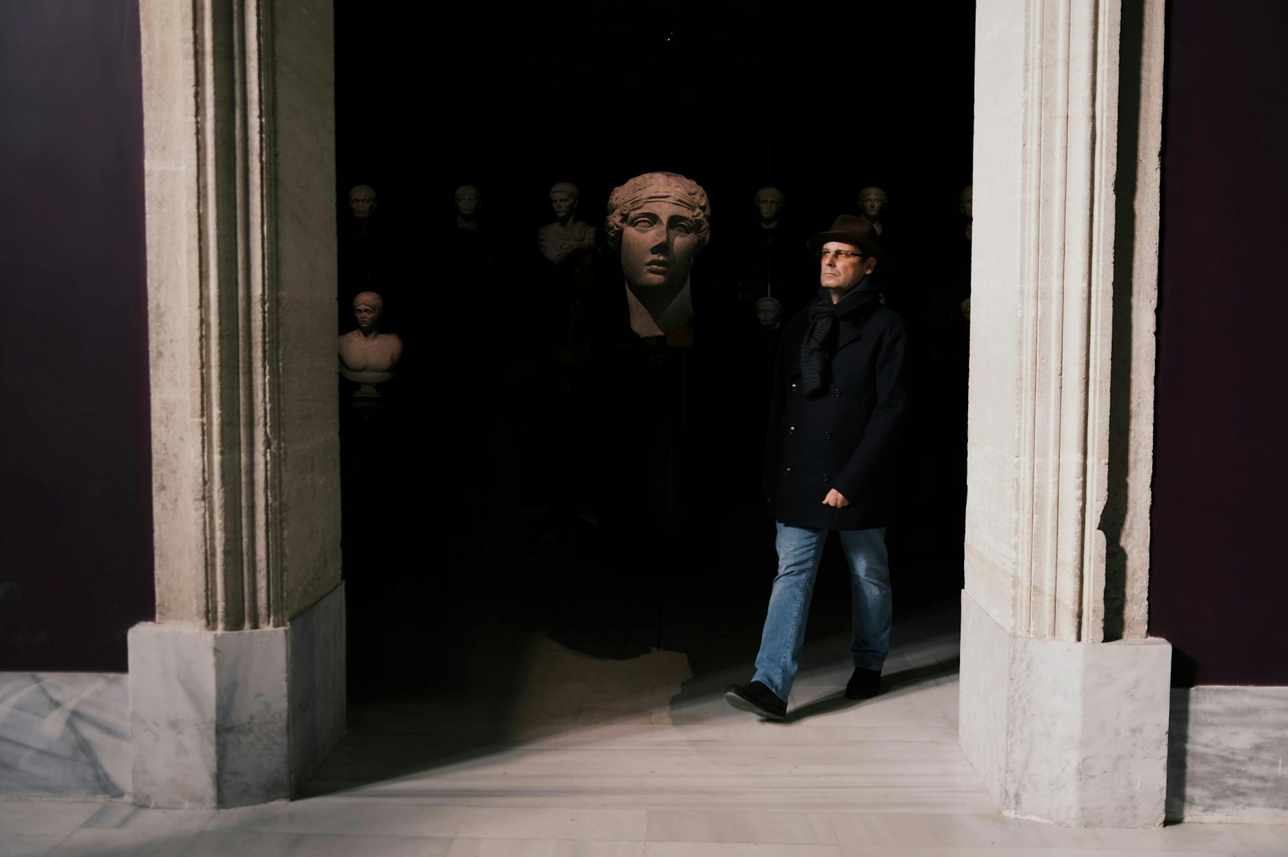페라 박물관의 어두운 전시실에서 관람객이 조각상 사이를 걸어가고 있습니다.